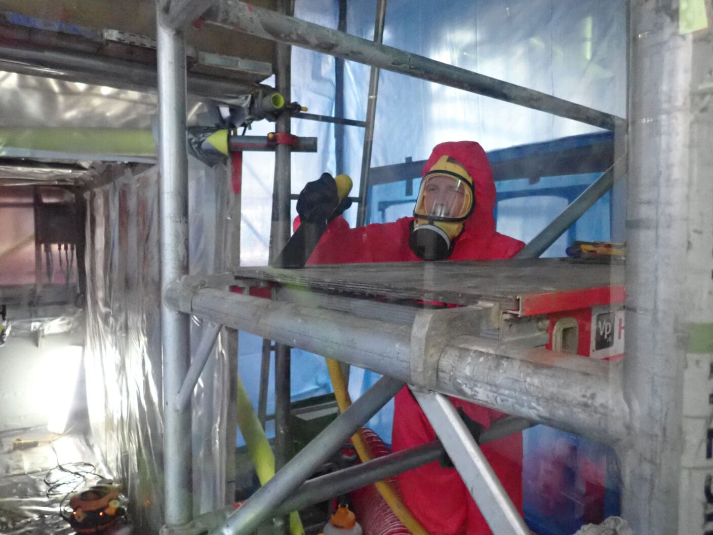 Man in a red suit and a mask removing asbestos from a building